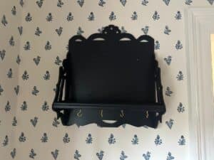Blue wall shelf with hooks, mounted on a white floral-patterned wallpapered wall.