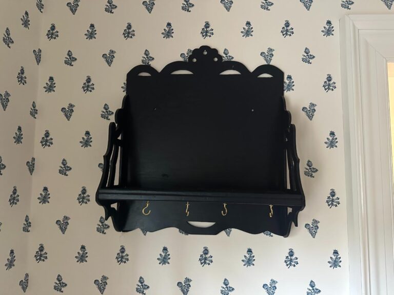 Blue wall shelf with hooks, mounted on a white floral-patterned wallpapered wall.