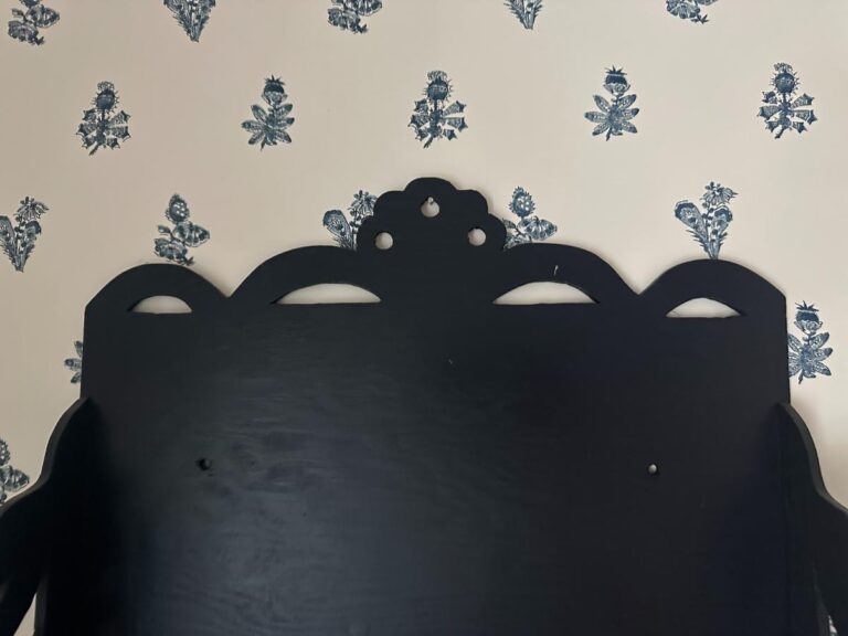 A Blue Wall Shelf / Bracket with a black decorative board contrasts against a white wall with a blue floral pattern.