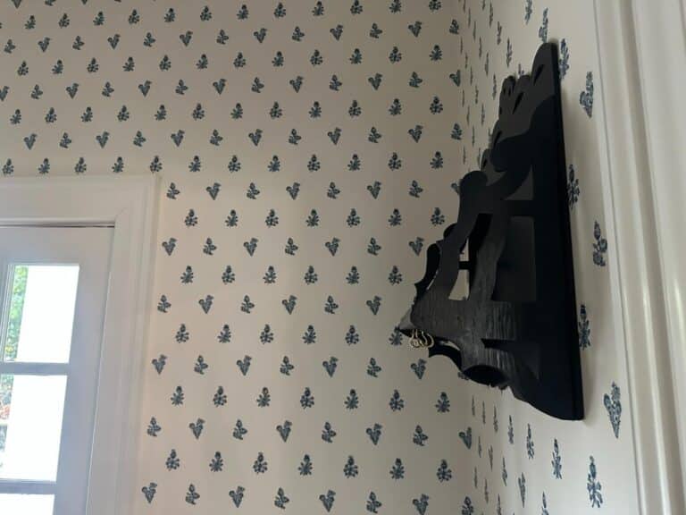 A wall adorned with floral-patterned wallpaper features a white door on the left and a decorative Blue Wall Shelf / Bracket attached to the wall.