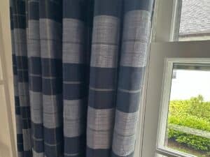 Blue Stripe Panels, Set of 6, hang next to a window revealing greenery and a building outside.