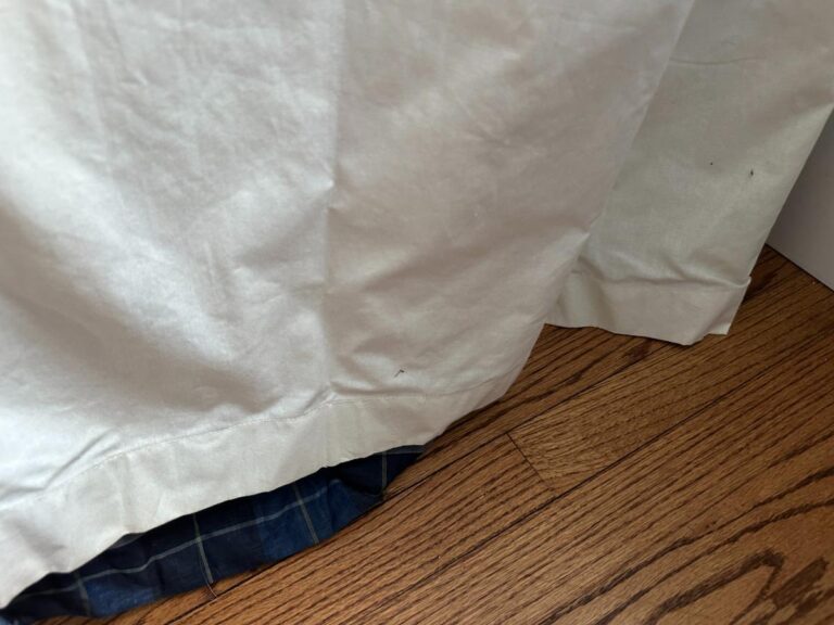 A white curtain hem gently touches the wooden floor, revealing a peek of the Blue Stripe Panels, Set of 6, underneath.