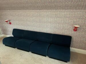 Room with a Herman Miller Blue Sectional, patterned wallpaper, and two red wall-mounted lamps.