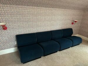 Herman Miller Blue Sectional set against a patterned wall with red sconces, on a beige carpeted floor.