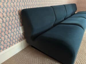 A Herman Miller blue sectional sits in a modern carpeted room with patterned wallpaper.