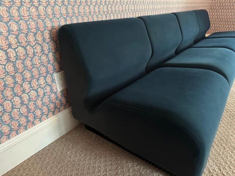 A Herman Miller blue sectional sits in a modern carpeted room with patterned wallpaper.