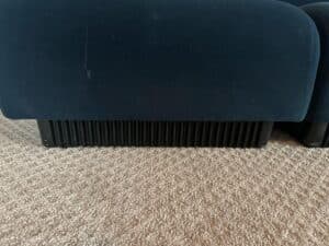 The base of a Herman Miller Blue Sectional with ribbed legs on a beige carpet.