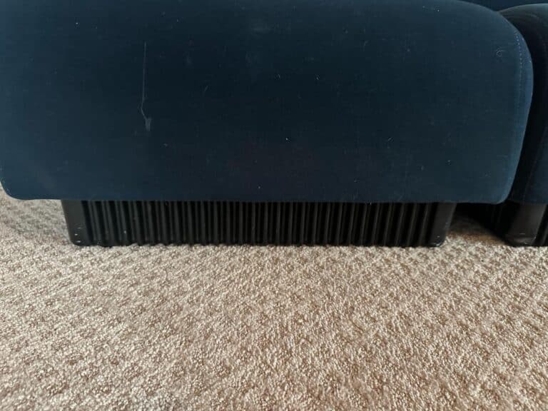 The base of a Herman Miller Blue Sectional with ribbed legs on a beige carpet.