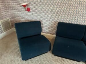 A Herman Miller Blue Sectional in a room with patterned wallpaper and a red wall lamp above it.