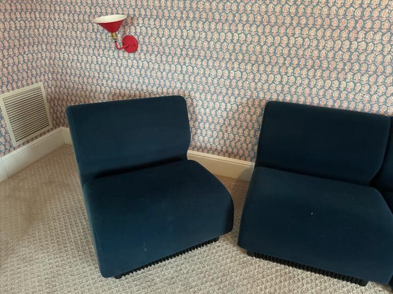 A Herman Miller Blue Sectional in a room with patterned wallpaper and a red wall lamp above it.