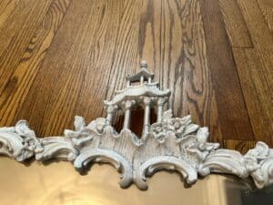 Close-up of a Vintage Chinoiserie Mirror featuring white carved floral and pagoda designs, placed on a wood floor.