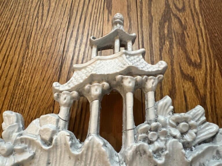Vintage Chinoiserie Mirror featuring a ceramic pagoda design with floral details against a wooden background.