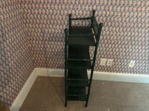 The Green Painted Bamboo Etagere, characterized by its tall and narrow design, is set against a floral wallpapered wall on a carpeted floor.