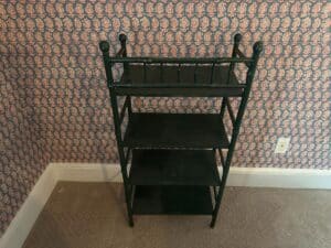 The Green Painted Bamboo Etagere stands with its three tiers and decorative top against patterned wallpaper and beige carpet.