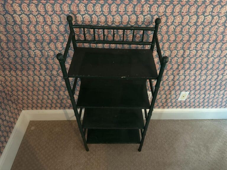 A compact green painted bamboo etagere with four shelves set against patterned wallpaper.