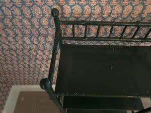 Green painted bamboo etagere in a room with patterned wallpaper featuring red and white motifs on a blue background.