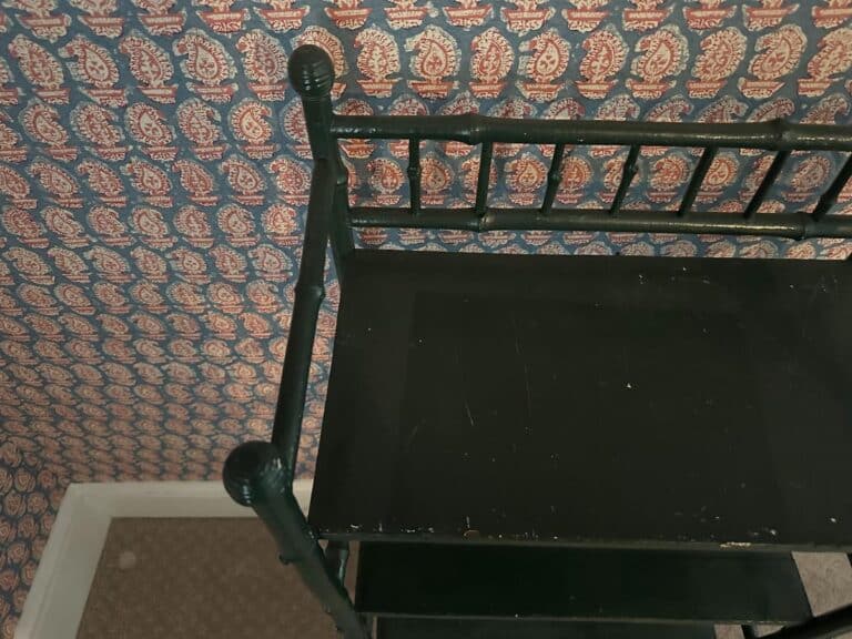 Green painted bamboo etagere in a room with patterned wallpaper featuring red and white motifs on a blue background.