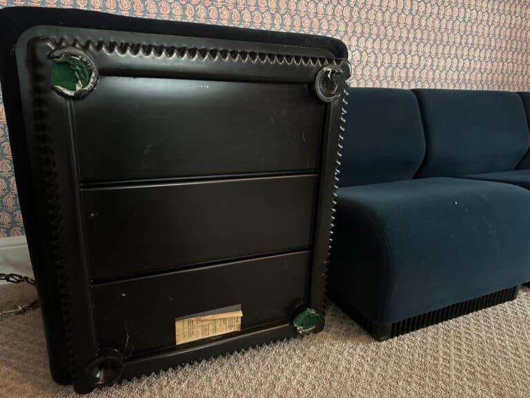 A black table stands beside a Herman Miller Blue Sectional sofa in a room with patterned wallpaper and a carpeted floor.