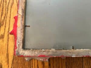 Close-up of a weathered, partially rusted metal frame on the wooden surface of a Vintage Chinoiserie Mirror.