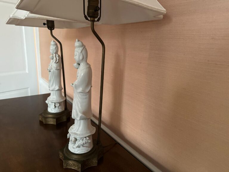 A pair of elegant Blanc De Chine Figural Lamps with white bases and square shades placed on a wooden surface.