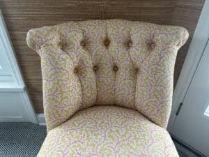 The Petite Tufted Back Side Chair on Casters, featuring floral upholstery and a button-tufted backrest, sits atop patterned carpeting in a bright room.
