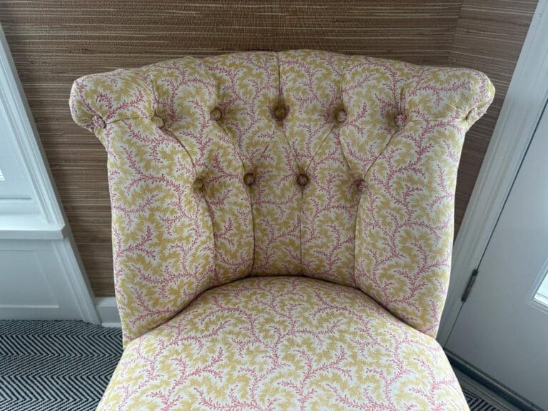 The Petite Tufted Back Side Chair on Casters, featuring floral upholstery and a button-tufted backrest, sits atop patterned carpeting in a bright room.