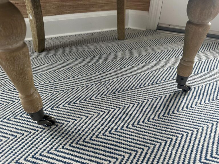 A Petite Tufted Back Side Chair on Casters with wooden legs is placed on a blue and white chevron-patterned rug.