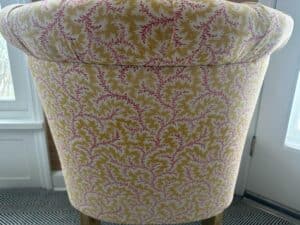 Sunlight fills the room, illuminating the back of a cushioned Petite Tufted Back Side Chair on Casters adorned with vibrant leaf-patterned fabric.