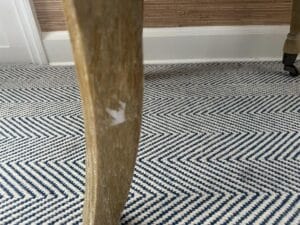 A close-up view of the Petite Tufted Back Side Chair on Casters reveals its wooden leg with a chipped surface, set on a blue and white chevron-patterned carpet.