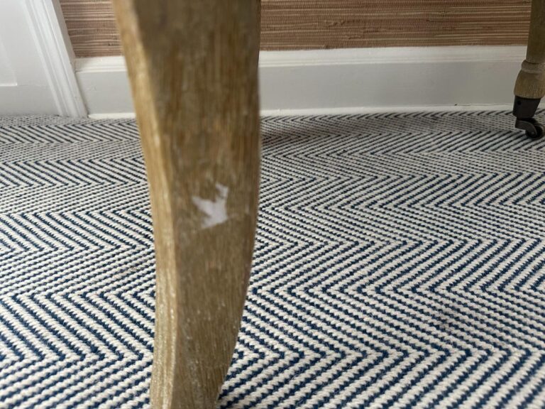 A close-up view of the Petite Tufted Back Side Chair on Casters reveals its wooden leg with a chipped surface, set on a blue and white chevron-patterned carpet.