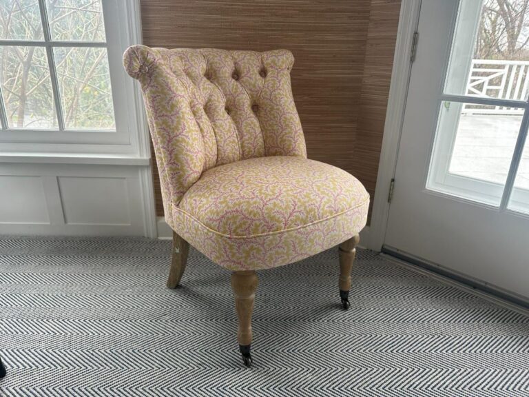 The Petite Tufted Back Side Chair on Casters, in pink with wooden legs, is placed on a patterned rug near a window and door.