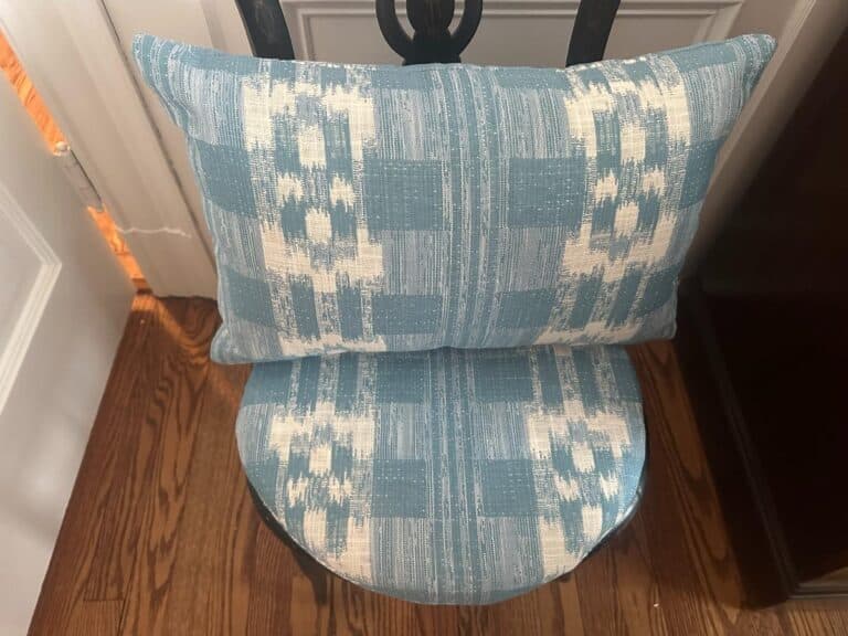 A wooden chair featuring a blue and white patterned cushion paired with Sister Parish Mahalo Print Pillows.