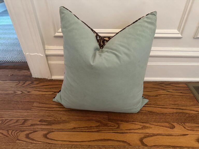 A Cut Velvet Leopard Pillow in light blue with patterned edges lies on a wooden floor near a white wall.