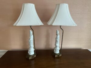A pair of Blanc De Chine Figural Lamps with ornate bases and white fabric shades on a wooden surface.