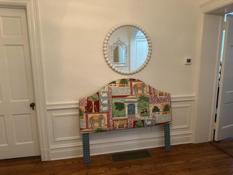 The Jane Churchill for Cowtan & Tout Indian Summer Full Size Headboard, featuring colorful animal prints, is set below a round mirror on a white wall with a wooden floor.