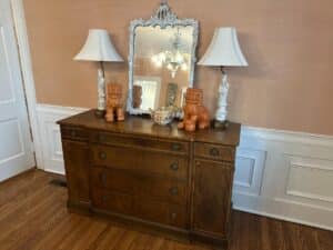 Vintage Chinoiserie Mirror on wooden dresser, flanked by two white lamps, with orange lion statues and a decorative bowl on top.