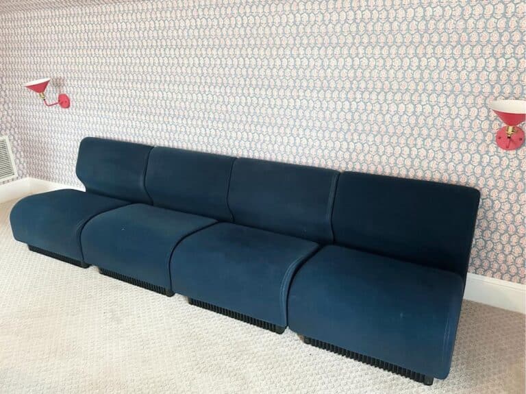 The Herman Miller Blue Sectional sits on light carpet against a patterned wallpaper, flanked by red wall lights.