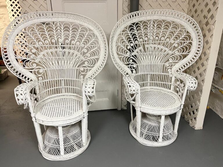A pair of Vintage Hollywood Regency Style Peacock Chairs, showcasing intricate white wicker patterns, stand against a white wall.