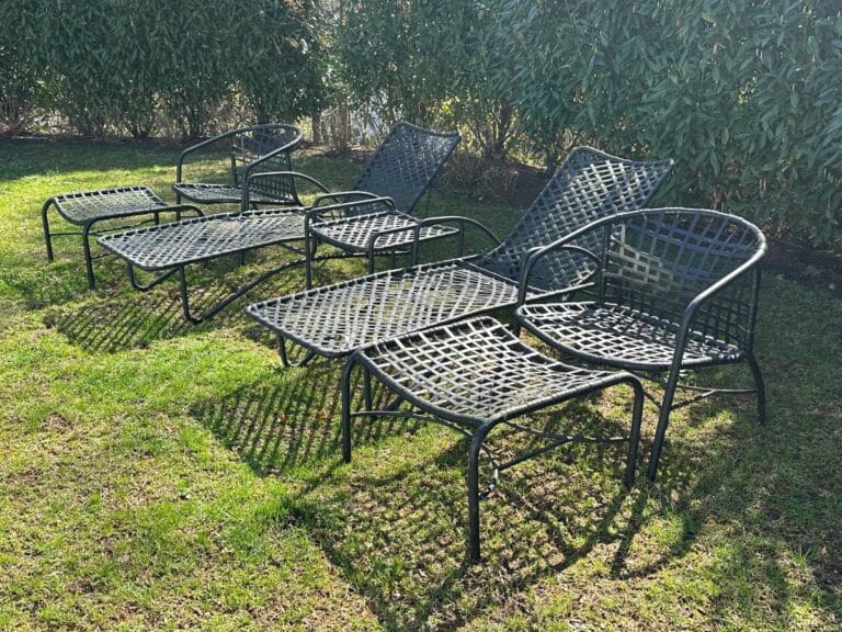 Five chairs from the Vintage Outdoor Brown Jordan Lounge Set, each with a footrest, sit on a grassy lawn surrounded by lush green shrubs.