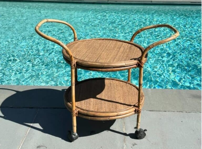A Vintage Rattan Bar Cart with wheels is set beside a crystal-clear blue swimming pool.