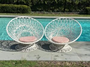 A pair of Vintage Spun Outdoor Chairs with pink cushions sit by a clear blue swimming pool on a sunny patio.