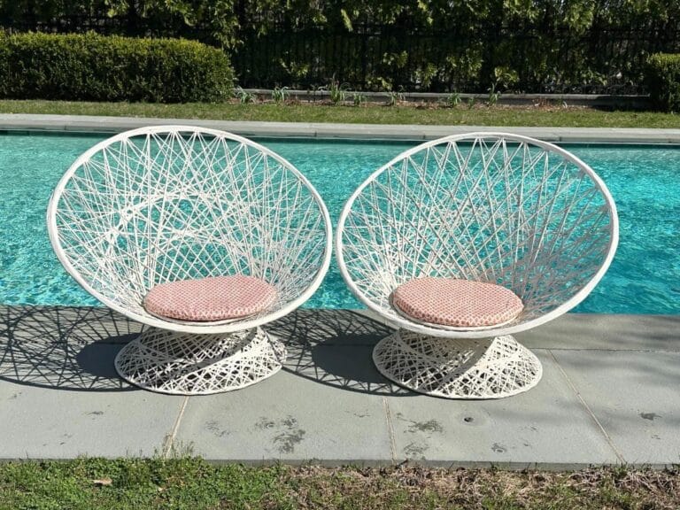 A pair of Vintage Spun Outdoor Chairs with pink cushions sit by a clear blue swimming pool on a sunny patio.