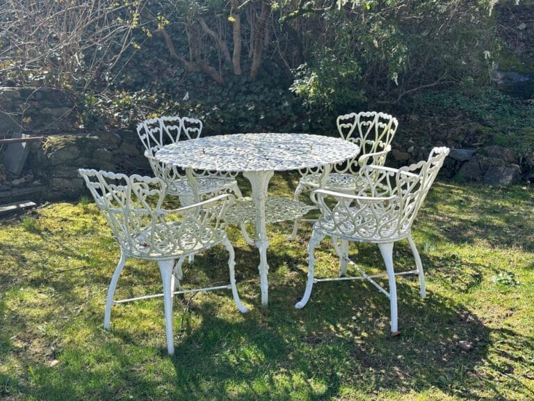 White Cast Iron Garden Furniture set of a table and four chairs on grass, surrounded by greenery.