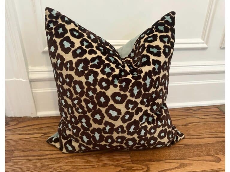 The Cut Velvet Leopard Pillow with blue accents is displayed against a white wall and wooden floor.