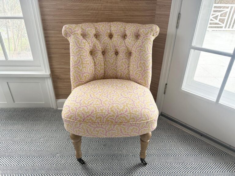 The Petite Tufted Back Side Chair on Casters, featuring a pink and yellow pattern, rests on a patterned rug near a window and door.