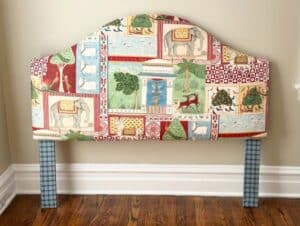The Custom Jane Churchill for Cowtan & Tout Indian Summer Headboard features animal-themed patchwork fabric and blue plaid legs, set against a beige wall and wooden floor.