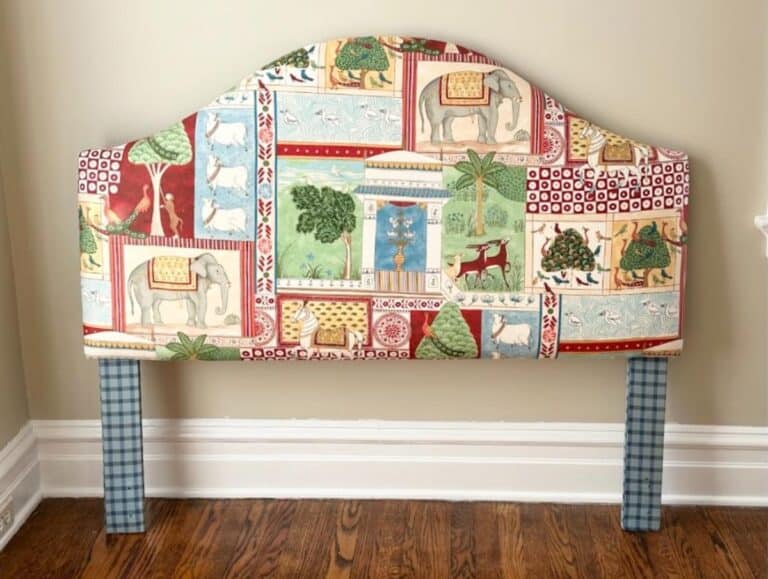 The Custom Jane Churchill for Cowtan & Tout Indian Summer Headboard features animal-themed patchwork fabric and blue plaid legs, set against a beige wall and wooden floor.