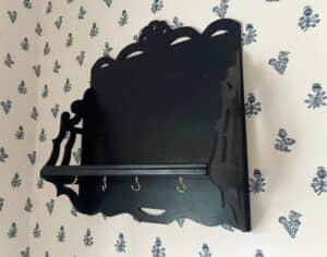 Blue wall shelf with hooks against a floral-patterned wallpaper background.