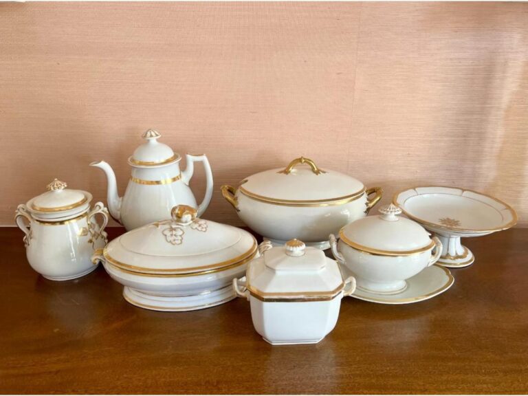 The Gold & White Serving Collection by Various Makers is elegantly displayed on a wooden surface with a beige background.
