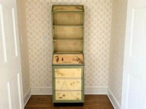A tall, vintage Hand Painted Secretary Desk with Bookcase showcases nature scenes, set against patterned wallpaper on a wooden floor.